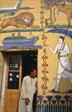 EGYPT,  , Luxor, Man at door of tourist shop decorated with mock hieroglyphics depicting the 20th