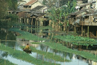 VIETNAM, Central, Hue, Wooden houses raised on stilts above waterway with man in small canoe in