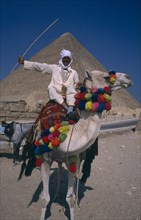 EGYPT,  Cairo Area, Giza, Man on camel in front of Pyramid