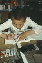 CHINA, Ningxia Province, Writing, Boy practising writing Chinese characters in shop owned and run