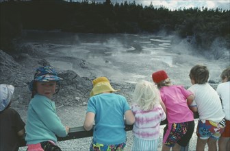 NEW ZEALAND, North Island, Waiotapu, Mud Pool with kids leaning against fence.