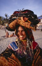 INDIA, Kerala, Kovalam, Portrait of a beach cloth vendor carrying her wares on her head