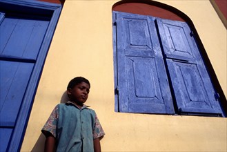 INDIA, Kerala, Kochin , Angled view of a boy standing by a yellow house with a blue door and window