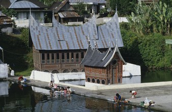 INDONESIA, Sumatra, Minankabu house with people washing clothes in the lake outside