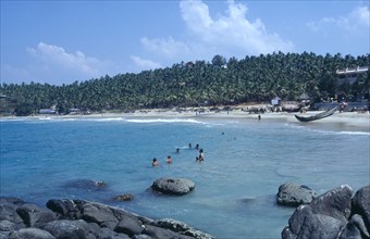 INDIA, Kerala, Kovalam, View from rocky outcrop over bay toward beach surrounded by palms with