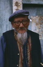 CHINA, Yunnan, Baisha , Portrait of a Naxi man with cap and glasses