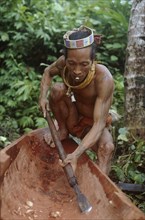 INDONESIA, Sumatra, Siberut Island, A Mentawi man hollowing out a canoe whilst he smokes a hand