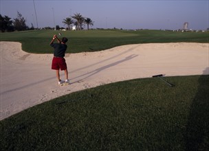 QATAR, Doha, Doha Golf Club.  Male golfer playing out of a bunker on short nine hole floodlit