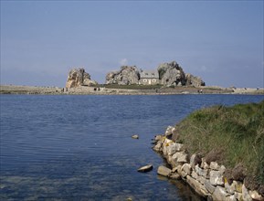 FRANCE, Brittany , Plougrescant, Overlooking an expanse of water to a house surrounded by rocks.