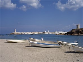 OMAN, Sur , Harbour with boats pulled up on stretch of sand with town and hilltop tower behind.
