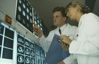 HEALTH, Hospital, Male and female doctors examine brain scans on wall mounted light boxes