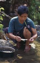 THAILAND, North, Mae Sariang, Karen refugee woman washing food while smoking a pipe