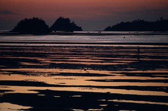 MALAYSIA, Borneo, Sabah, Kinarut Beach. Sunset reflected in the water with silhouetted islands just