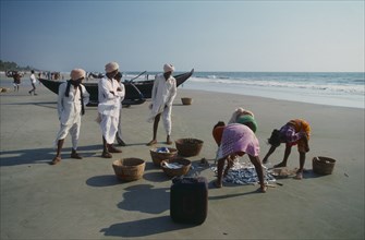 INDIA, Goa, Colva , Three men in turbans watch three women sorting the morning catch near a boat on