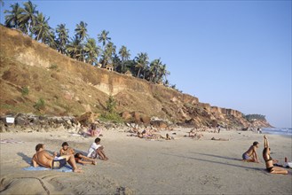 INDIA, Kerala, Varkala, Sun bathers on sandy beach surrounded by small cliffs topped with palms