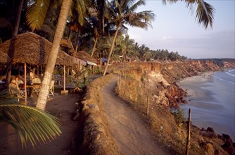 INDIA, Kerala, Varkala , Coastal path along cliff tops with sandy beach below and woman sitting