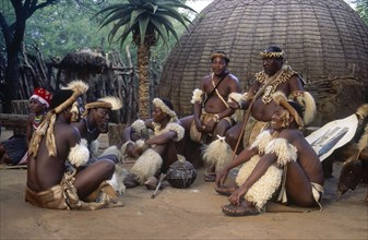 SOUTH AFRICA, KwaZulu Natal, Tribesmen sitting on the ground outside a hut whilst the chief sits on