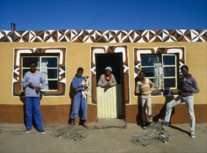 SOUTH AFRICA, Tribal Peoples, Basotho family outside typical painted home. young boys with model