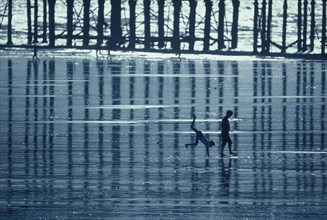 ENGLAND, East Sussex, Hastings, Two boys playing on the beach at low tide beside the pier