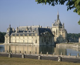 FRANCE, Nord Picardy, Oise, Chantilly Chateau with its reflection in surrounding water and a road