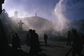 10122739 TIBET   Lhasa Jokhung Square.  People silhouetted in sunlight through smoke.