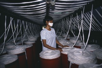 CAMBODIA, Kampong Cham, Woman surrounded by vats of yarn in textile factory.