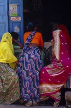 INDIA, Rajasthan , Devargh, Women with backs to camera sitting at shop entrance.