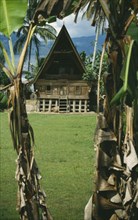 INDONESIA, Sumatra, Lake Toba , Wooden Batak house with pointed roof on Samosir Island seen through