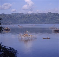 INDONESIA, Lombok, Lembar, Bamboo fishing platforms in the sea with a man in a canoe rowing towards