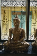 THAILAND, Bangkok, Seated Buddha covered with gold leaf in front of window with decorative metal