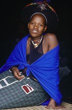 SOUTH AFRICA, KwaZulu Natal, Msinga, Zulu woman in bright clothing sitting on the ground