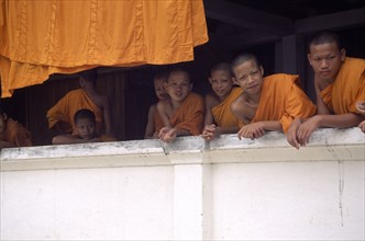 LAOS, Luang Prabang, Young monks leaning over monastery wall.