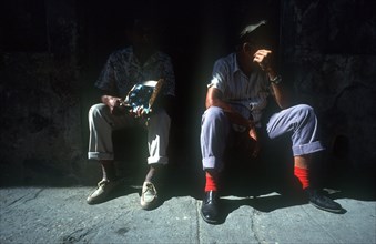 CUBA, Havana , Two men sitting on a doorstep cast in shadow