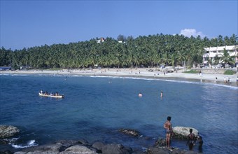 INDIA, Kerala , Kovalam Beach, View of beach with people swimming and a canoe.