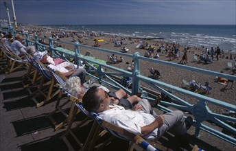 ENGLAND, East Sussex, Brighton , View over people in deckchairs lining the promenade toward the