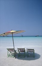 THAILAND, Pattaya , Coral Island, Empty sun loungers and umbrella on beach with boats moored just