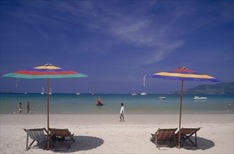 THAILAND, Phuket, Patong Beach, Empty deckchairs and sun parasols on the beach with people walking