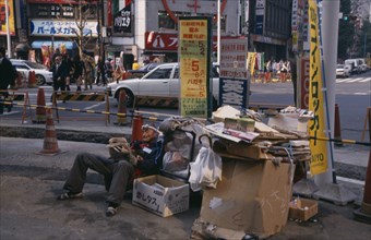 JAPAN, Honshu, Tokyo, Homeless man living on the street with his cardboard home at a busy road