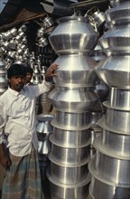 BANGLADESH, Dhaka , Vendor standing beside stack of vessels at tinware stall in market.