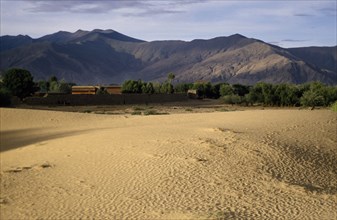 CHINA , Tibet  , Samye, Wind rippled encroaching sand with mountain backdrop.