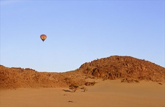 NAMIBIA, Namib Desert, Hot air ballooning above rocky outcrop over sand dunes