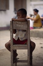 THAILAND, North, Mae Sai , Karen refugee boy sitting on chair