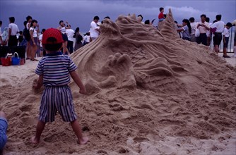 SINGAPORE, Beach, Sand sculpture of a Dragon with a boy standing in front of it holding a handful