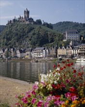 GERMANY, Rhineland, Cochem, Hilltop castle overlooking houses beside the Mosel River with flowers