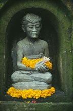 INDONESIA, Bali, Ubud, Small Hindu shrine detail of seated figure with flower offerings in the Miro