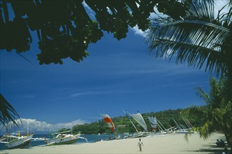 INDONESIA, Lombok, Senggigi, Outrigger fishing sailboats on the beach seen through trees