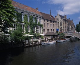 BELGIUM, West Flanders, Bruges, "Boats dock on the canal near a bridge, next to an ivy covered