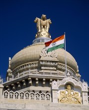 INDIA, Karnataka, Bangalore, "Vidhana Soudha building.  Exterior detail of roof dome, crest, flag