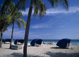 USA, Florida , Fort Lauderdale , Sunbathers sitting in blue Windbreaks on sandy beach lined with