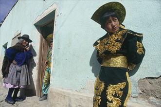 BOLIVIA, Potosi, Boy in costume in front of light green house with old woman standing by doorway